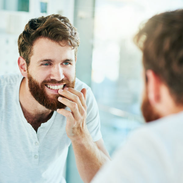 man looking at teeth in mirror